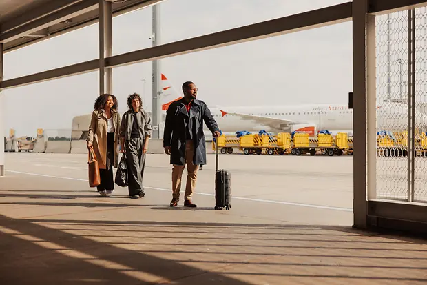 People with carry-on luggage in the outdoor area of Vienna International Airport on their way to the terminal.