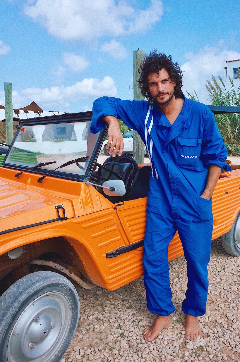 DJ and producer Wolfram wearing blue overalls in front of an orange car