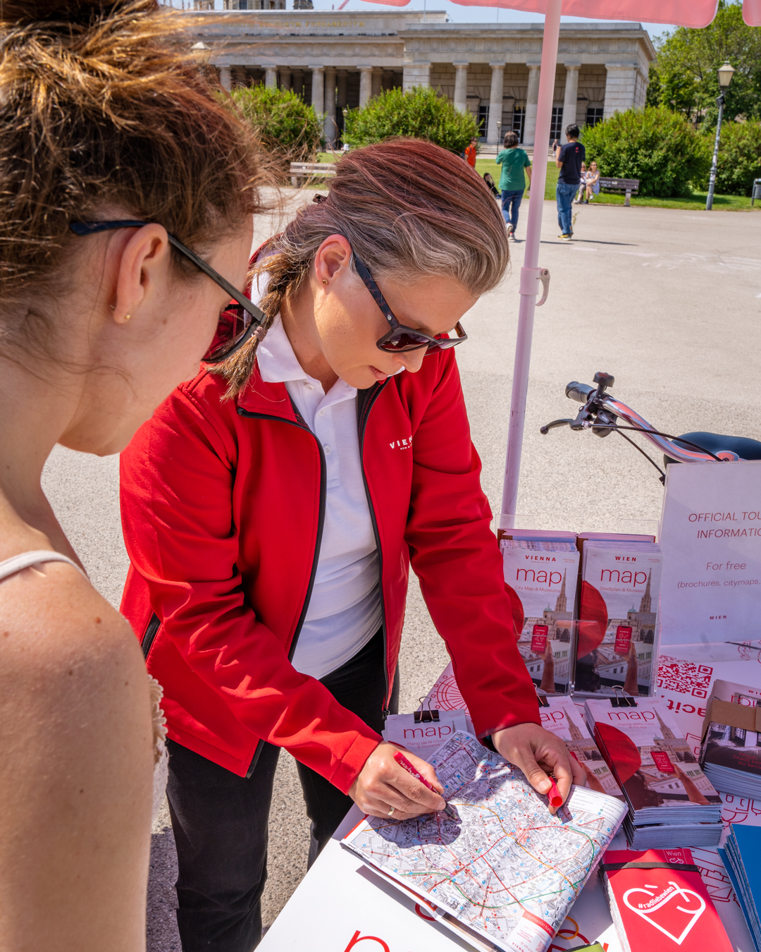 Servicio de información turística móvil con bicicleta de carga, una trabajadora le muestra algo a una clienta en el mapa de la ciudad