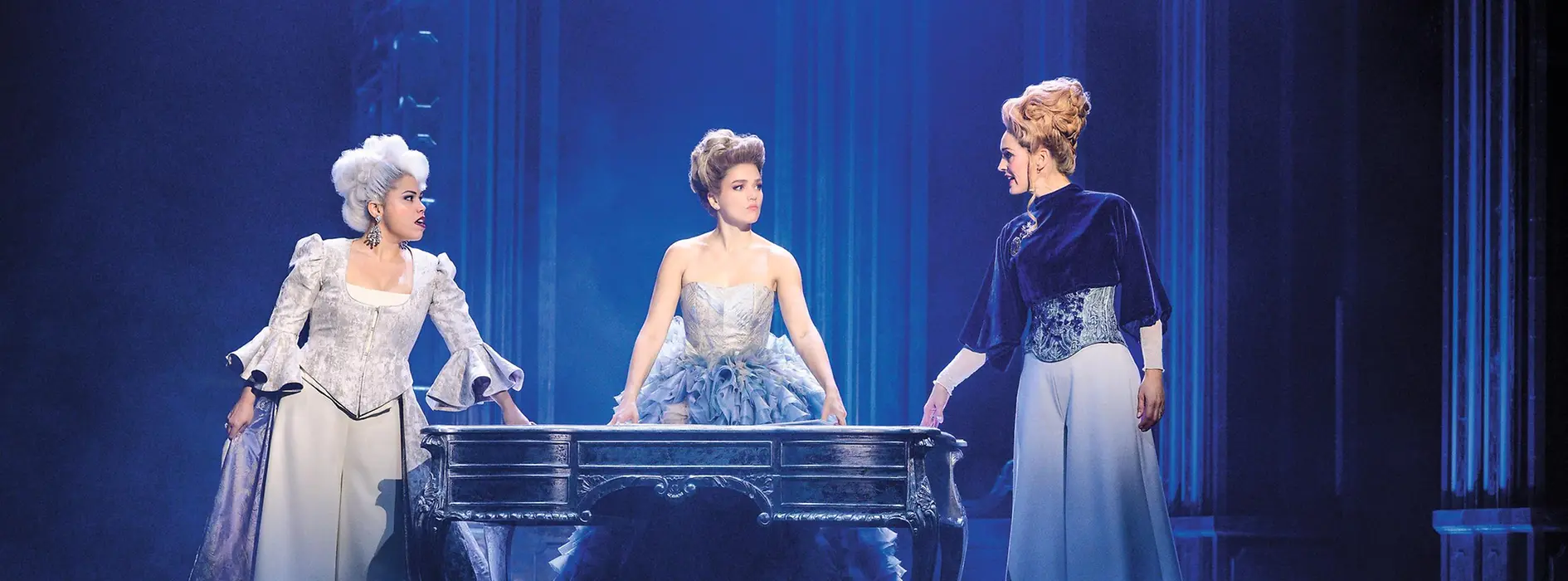 Maria Theresia steht mit ihrer Mutter und der Erzieherin und Vertrauten Gräfin Fuchs an einem antiken Schreibtisch.