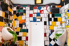 Künstlerisch gestaltete öffentliche Toilette mit bunter Mosaikverkleidung und organischen Formen nach Hundertwasser.
