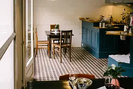 Kleines Restaurant mit Holztischen, gemustertem Fliesenboden und offener Küche.