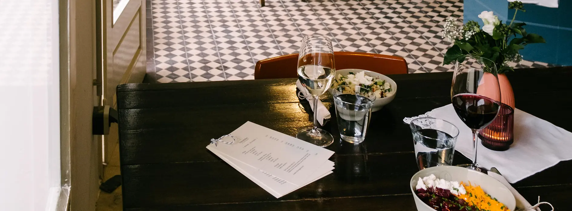 Kleines Restaurant mit Holztischen, gemustertem Fliesenboden und offener Küche.