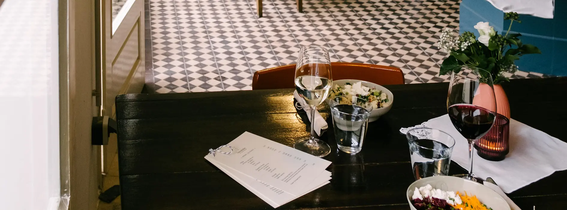 Kleines Restaurant mit Holztischen, gemustertem Fliesenboden und offener Küche.