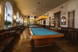 Historischer Billardsaal mit zwei Tischen, Holzvertäfelung und Queue-Wänden.