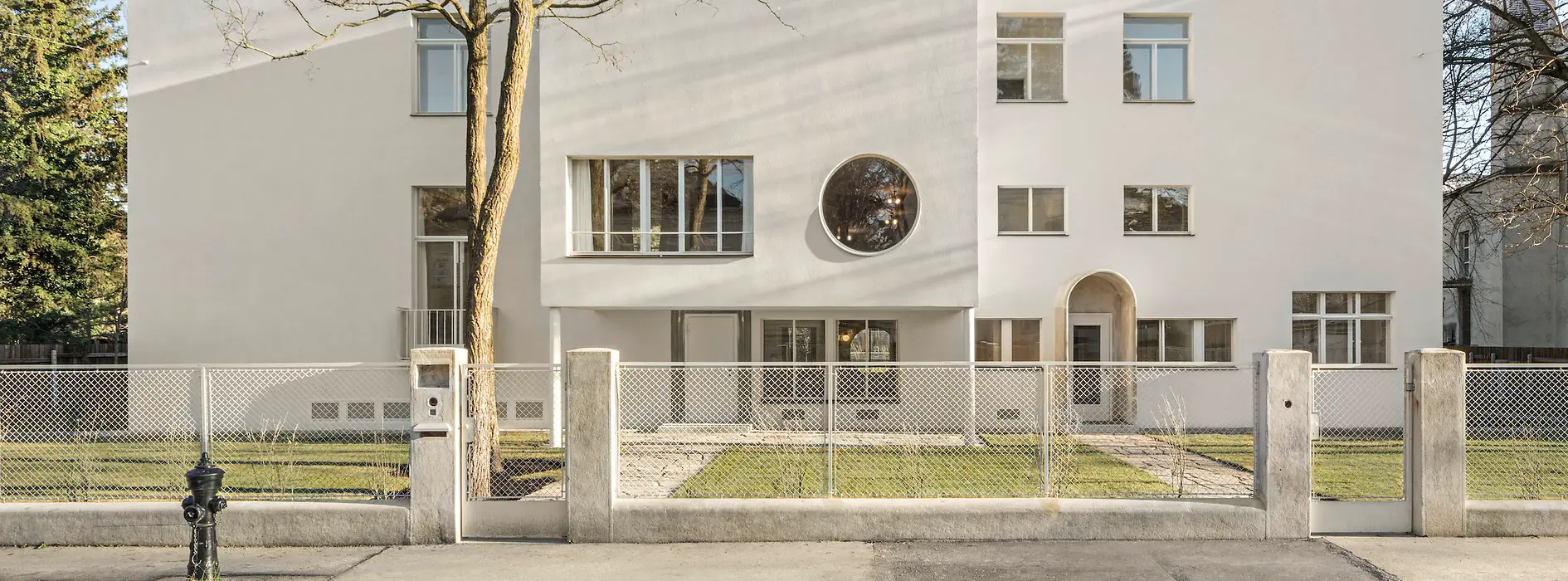 Straßenansicht der modernistischen Villa mit rundem Fenster und zurückgesetztem Eingang.