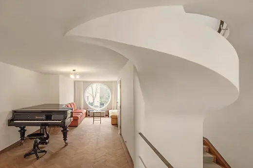Sala de música con piano de cola, ventana redonda y asientos.