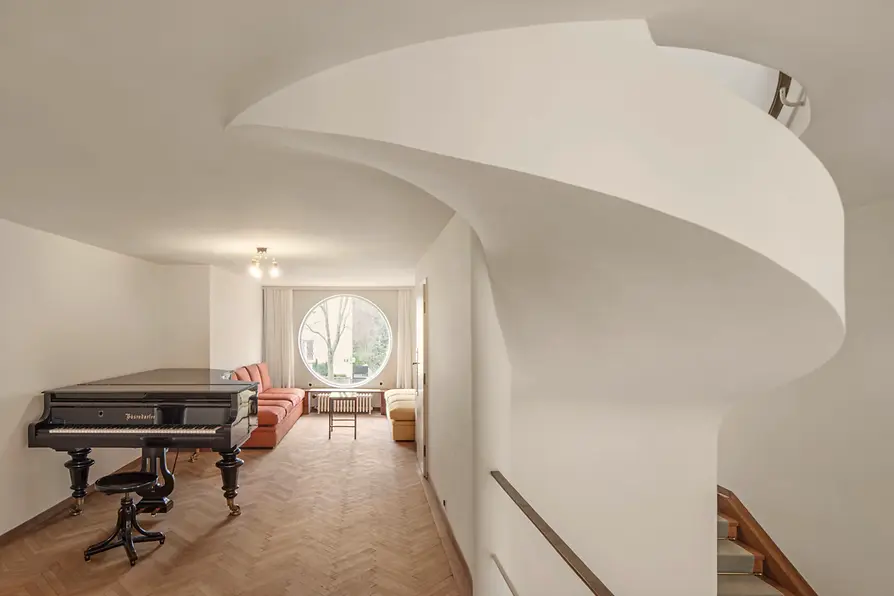 Sala de música con piano de cola, ventana redonda y asientos.