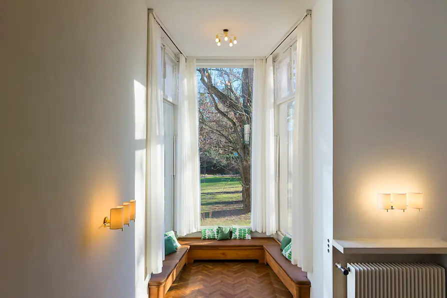 Interior luminoso con grandes ventanas, bancos empotrados y vistas al campo.