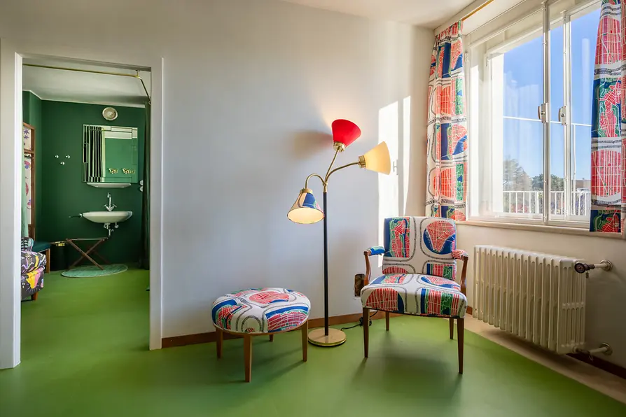 Rincón de descanso en la habitación de invitados con sillón estampado y lámpara de pie.