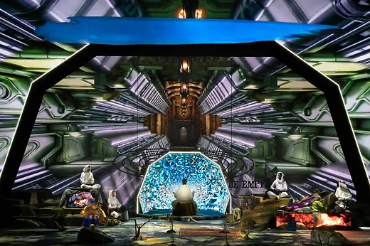Instalación escénica futurista con varias personas ante un fondo digital luminoso.