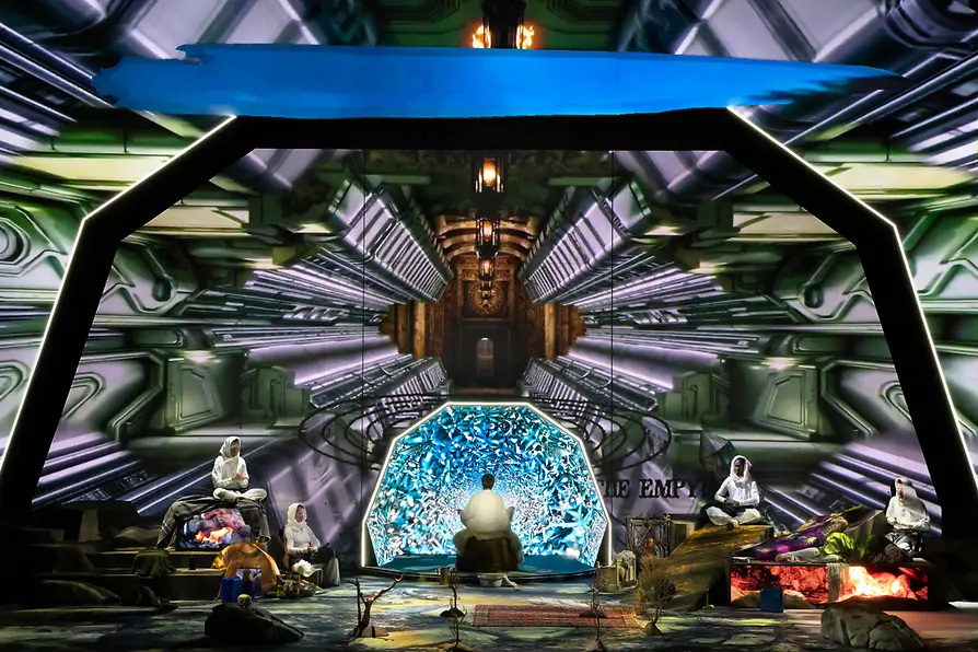 Instalación escénica futurista con varias personas ante un fondo digital luminoso.