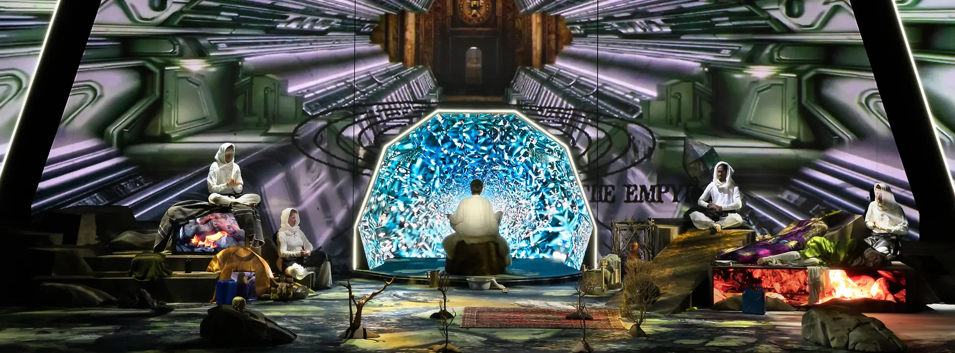 Futuristische Bühneninstallation mit mehreren Personen vor einem leuchtenden digitalen Hintergrund.