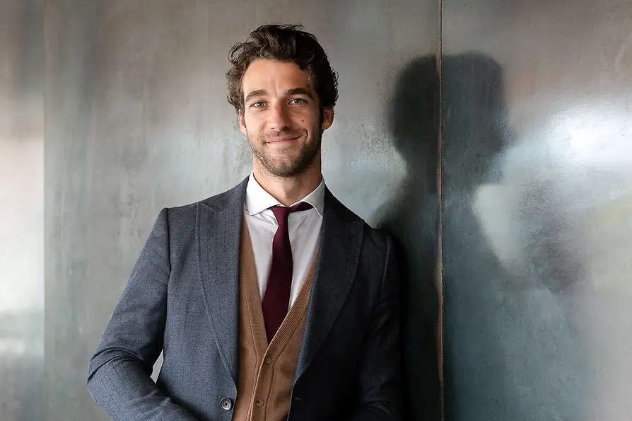 Lorenzo Viotti im Anzug, an einer Wand lehnend