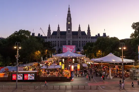 Blick auf die belebte Gastromeile beim Film Festival, dahinter das Wiener Rathaus.