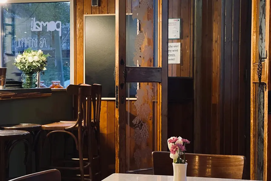 A bright dining room with wood-paneled walls, an open glass door, and small flower vases on simply set tables.