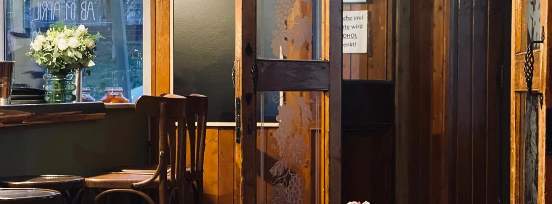 A bright dining room with wood-paneled walls, an open glass door, and small flower vases on simply set tables.