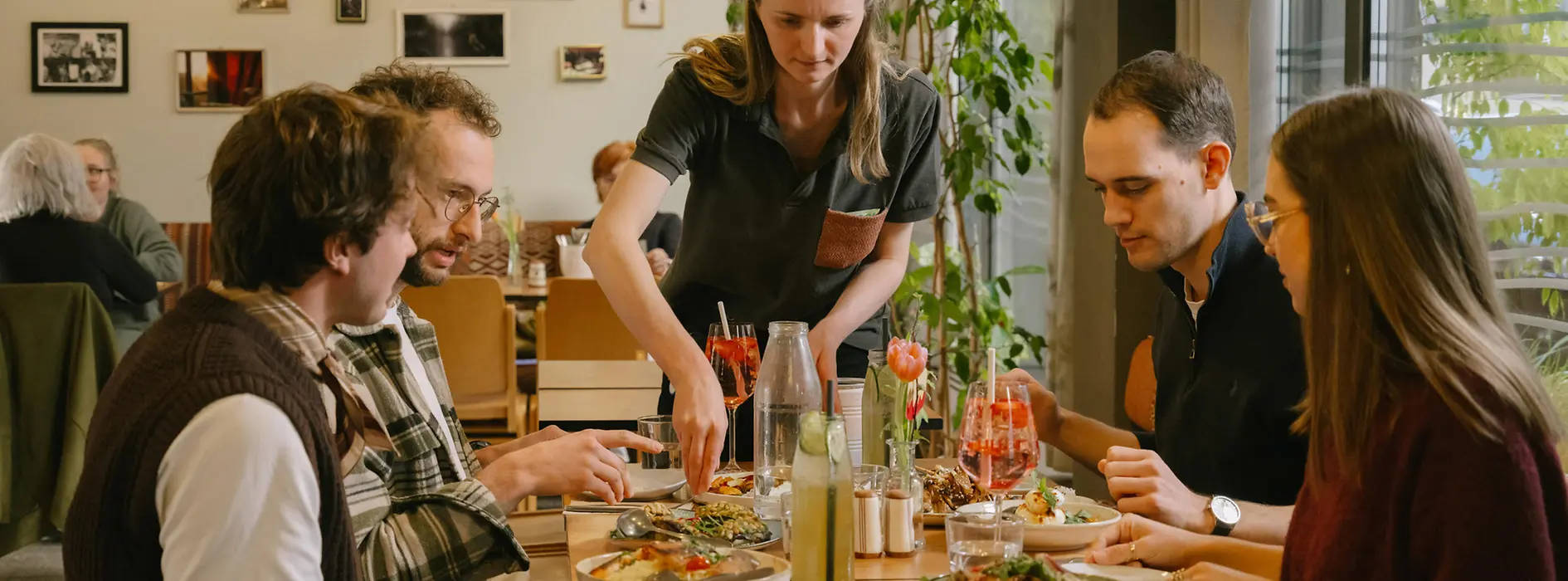 Guests are sitting together at a table at magdas Lokal, including a man using a wheelchair. The image shows an inclusive and accessible restaurant setting.