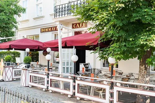 Gastgarten des Café Dommayer mit roten Sonnenschirmen und Sitzplätzen.