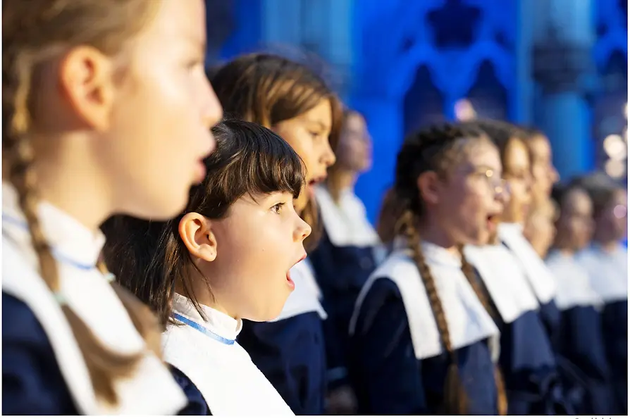 Las chicas del coro de Viena cantan en una misa, con uniforme blanco y azul.