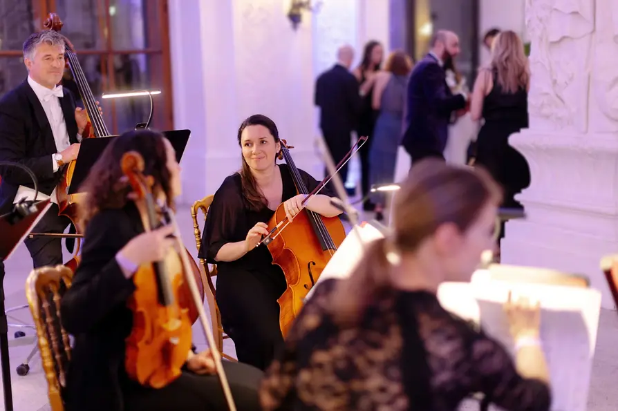Tanzpause beim Petite Vienna Ball: Das Streichquartett plaudert, dahinter stehen Ballgäste und unterhalten sich.