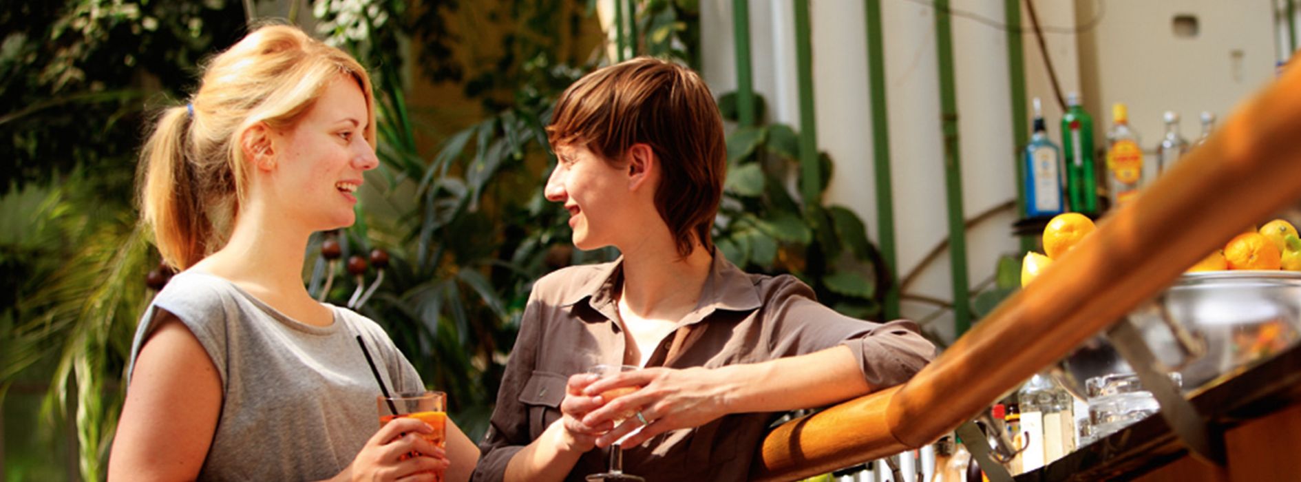 Две молодые женщины с напитками, стоящие и болтающие возле бара