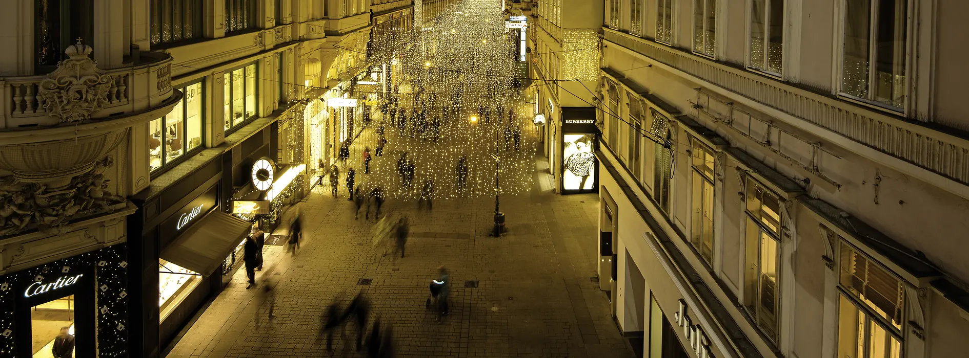 Gente a passeggio di notte nella piazza Kohlmarkt suggestivamente illuminata