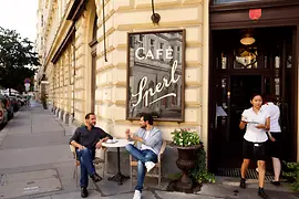 Dwaj mężczyźni siedzący przed kawiarnią 