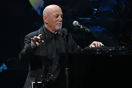 Billy Joel penché sur son piano, le micro devant lui.