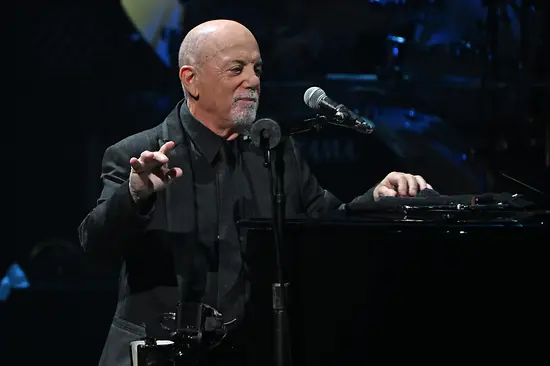 Billy Joel appoggiato al pianoforte, davanti a sé il microfono.