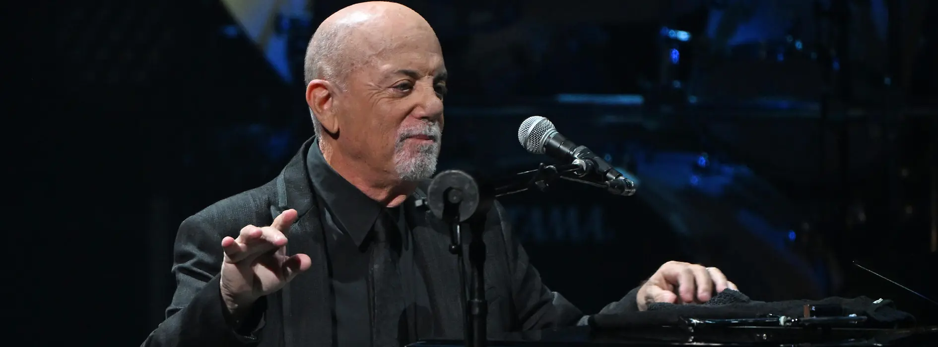 Billy Joel penché sur son piano, le micro devant lui.
