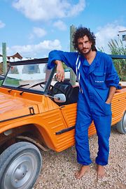 DJ and producer Wolfram wearing blue overalls in front of an orange car