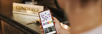 Mężczyzna stoi przed recepcją z otwartą aplikacją ivie na swoim telefonie komórkowym