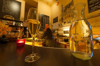 Szigeti pezsgőbolt, belső nézet egy pohár pezsgővel és vendégekkel 