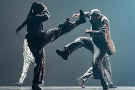 Mette Ingvartsen: Rush. A dancer wrapped in metal foil leans on a white table.