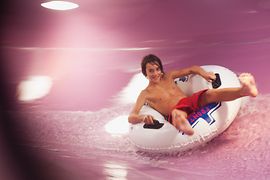 Мальчик на круге, скатывающийся с водной горки в термальном комплексе Therme Wien