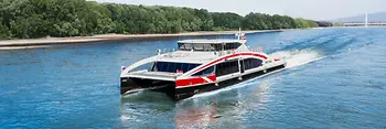 Il catamarano ad alta velocità Twin City Liner naviga sul Danubio con la foresta alluvionale sullo sfondo.