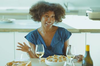 A woman at a table with a wine glas, a bottle and a plate of escargots
