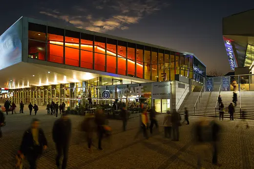 Wiener Stadthalle, di sera illuminata da luci gialle e rosse, visitatori