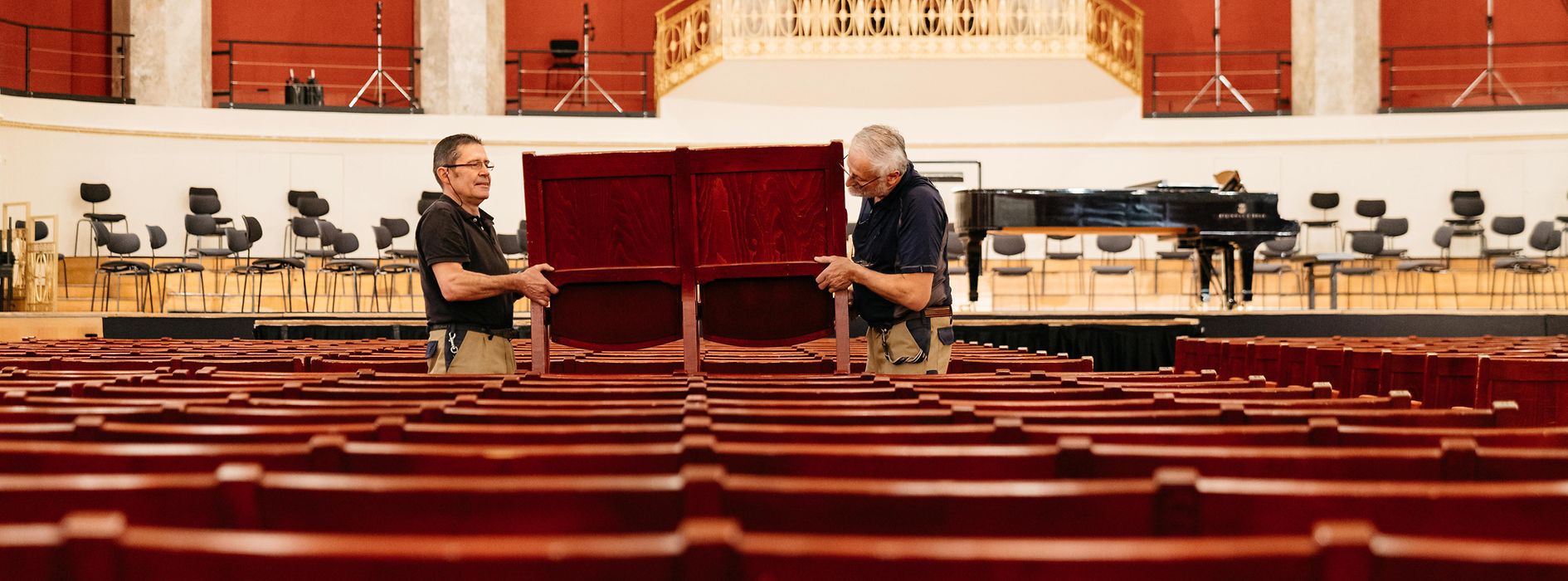 Wolfgang Becker and Franz Risavy, carpenters at the Wiener Konzerthaus, lift a bench in the Great Hall