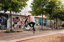 Skater in a public outdoor space with graffiti in the background.