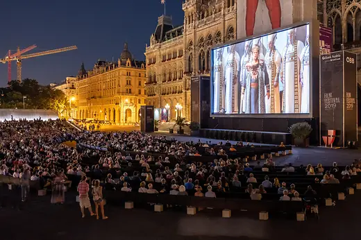 Filmfesztiválon a Rathausplatzon, sokan néznek filmet a kivetítőn.