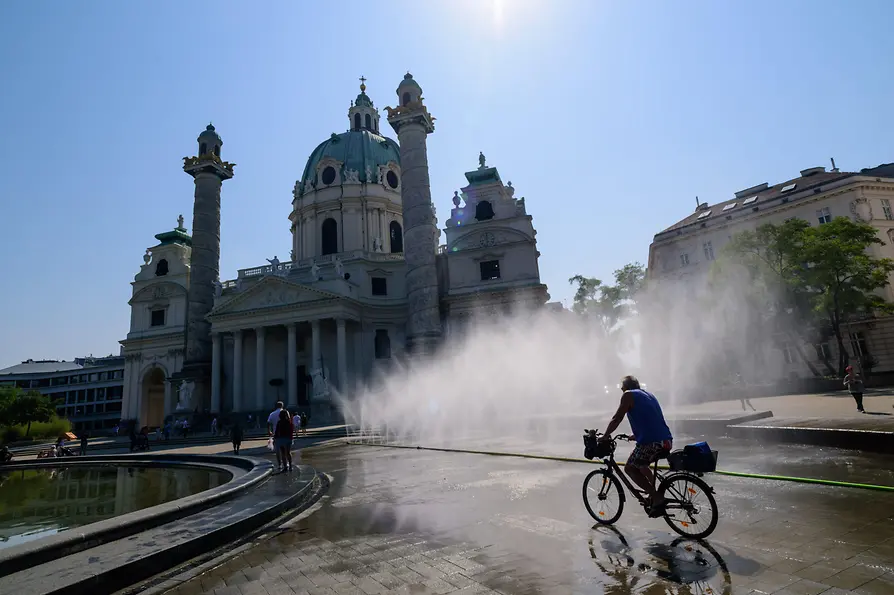 Radfahrer fährt durch Wasser-Sprühnebel vor der Karlskirche