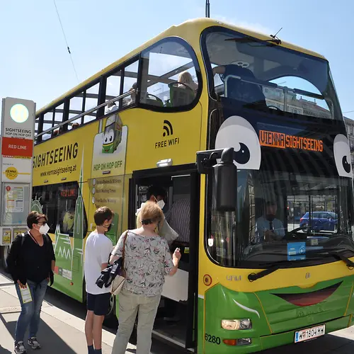 Several people getting on a yellow Hop-On Hop-Off double-decker bus of Vienna Sightseeing Tours