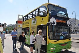 Több személy száll be egy sárga Hop-On Hop-Off kétszintes buszba, amelyet a Vienna Sightseeing Tours üzemeltet.
