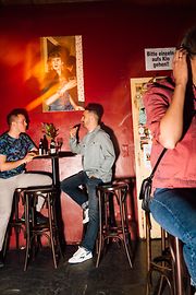 Двое мужчин разговаривают в баре Marea Alta, у барной стойки сидит женщина