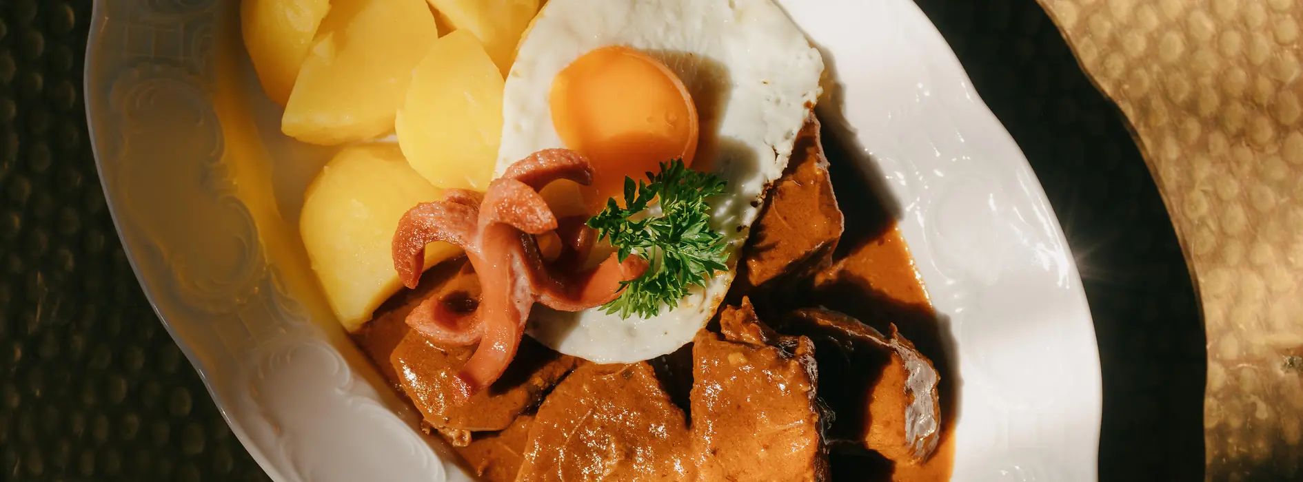 A plate of Fiakergulasch (goulasch) with boiled potatoes, fried egg, and a sausage