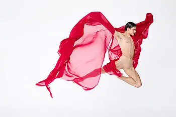 Danseur en plein saut, tenant dans chaque main un tissu rouge transparent qui flotte autour de lui.