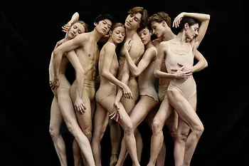 Seven ballet dancers standing close together in pose.