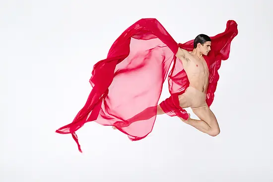 Dancer mid-jump holding a red, translucent cloth in both hands, fluttering around him.